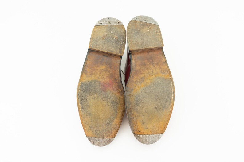 May include: Close-up of the soles of a pair of brown leather shoes. The soles are worn and have a textured pattern.