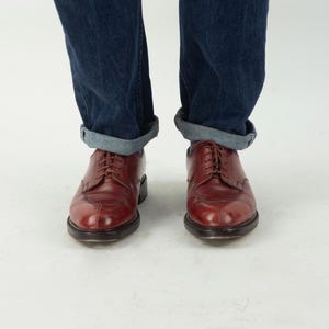 May include: A pair of brown leather lace-up shoes with a pointed toe. The shoes are worn with rolled up blue jeans.