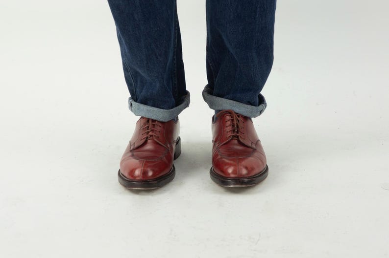 May include: A pair of brown leather lace-up shoes with a pointed toe. The shoes are worn with rolled up blue jeans.
