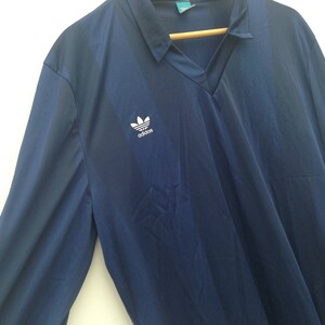 K&ouml;nnte beinhalten: Ein marineblaues Langarmhemd mit einem wei&szlig;en Adidas-Logo auf der linken Brust.