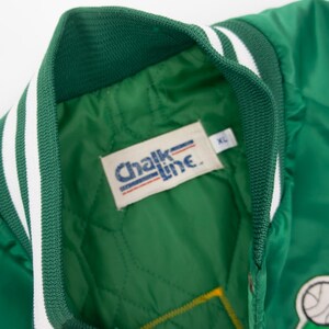 May include: Green satin bomber jacket with white and green striped trim. The jacket has a "Chalk Line" label with a size XL tag. The jacket has a green and white patch with a cartoon leprechaun holding a basketball.