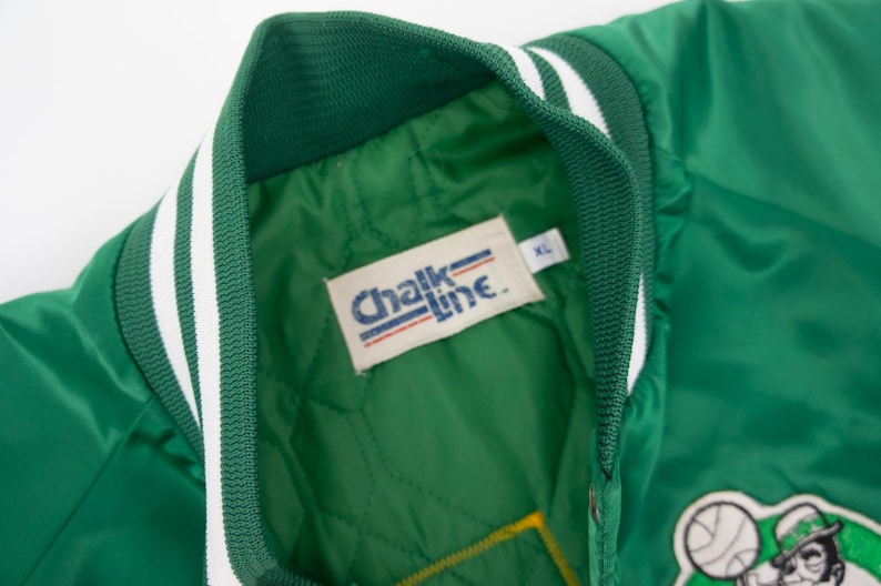 May include: Green satin bomber jacket with white and green striped trim. The jacket has a "Chalk Line" label with a size XL tag. The jacket has a green and white patch with a cartoon leprechaun holding a basketball.