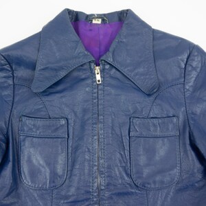 K&ouml;nnte beinhalten: Eine marineblaue Vintage-Lederjacke mit Kragen und zwei Vordertaschen. Die Jacke hat einen Rei&szlig;verschluss und ein lila Futter. Ein klassischer Stil.