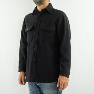 May include: A dark charcoal button-down shirt with two chest pockets. The shirt has a classic collar and is made of a textured fabric. The sleeves are long, and the shirt is worn with blue jeans. A casual, everyday garment.