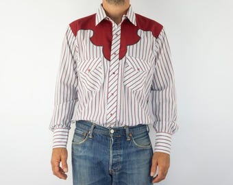 May include: A striped shirt in white and burgundy with long sleeves and a button-down design. It has burgundy shoulder details and two chest pockets. The person is wearing blue denim jeans.