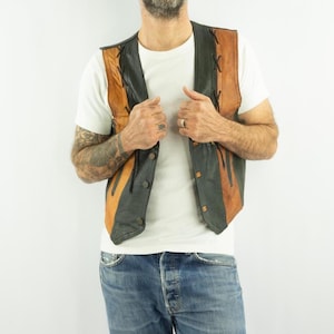 Puede incluir: Un chaleco de cuero vintage con un diseño bicolor. El chaleco presenta paneles negros y marrones con costuras decorativas y cierres de botones. Una prenda de vestir exterior clásica.