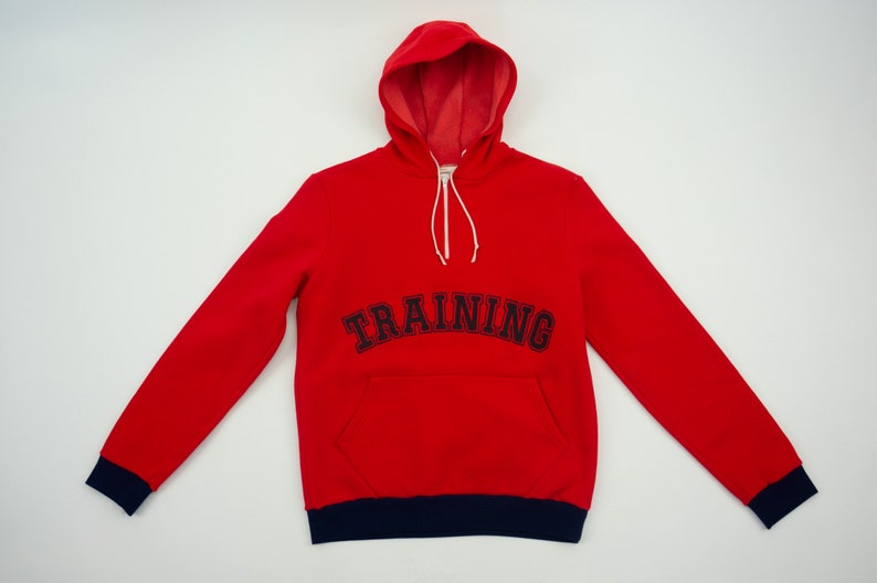 K&ouml;nnte beinhalten: Roter Kapuzenpullover mit dunkelblauem Saum und dem Wort "TRAINING" in dunkelblau auf der Vorderseite gestickt.