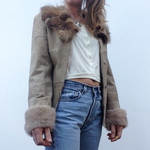 Peut inclure: Une veste en daim marron avec un col et des poignets en fourrure. La veste a une fermeture à boutons et un seul bouton sur chaque poignet.
