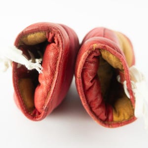 May include: Pair of vintage red leather boxing gloves with white laces. The gloves have a worn appearance, with visible stitching and a yellowed interior. The gloves are set against a white background.