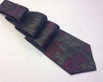 Puede incluir: Una corbata de seda verde oscuro con un patrón de elefantes rojos. Los elefantes son estilizados y tienen un aspecto texturizado.