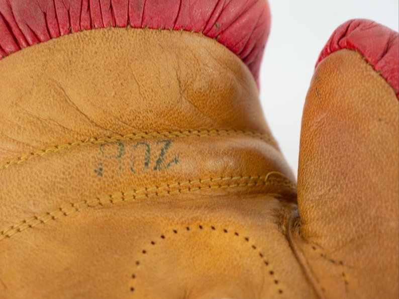May include: Close-up of a tan leather boxing glove with red trim. The glove has visible stitching and the number "8 OZ" is stamped on the leather. The image highlights the texture and detail of the glove's construction.