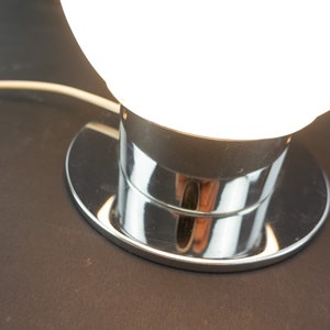 May include: A chrome table lamp with a white glass globe shade. The lamp has a round base and a chrome stem.