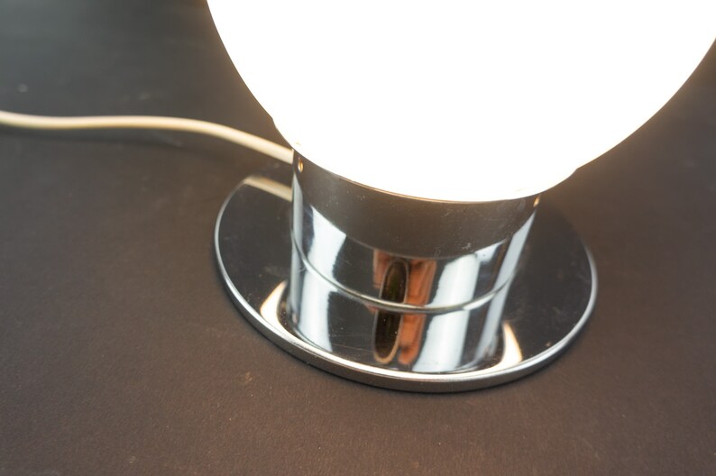 May include: A chrome table lamp with a white glass globe shade. The lamp has a round base and a chrome stem.