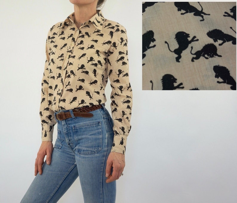 May include: A beige long-sleeved button-down shirt with a black lion print. The shirt has a classic collar and a button-up front.