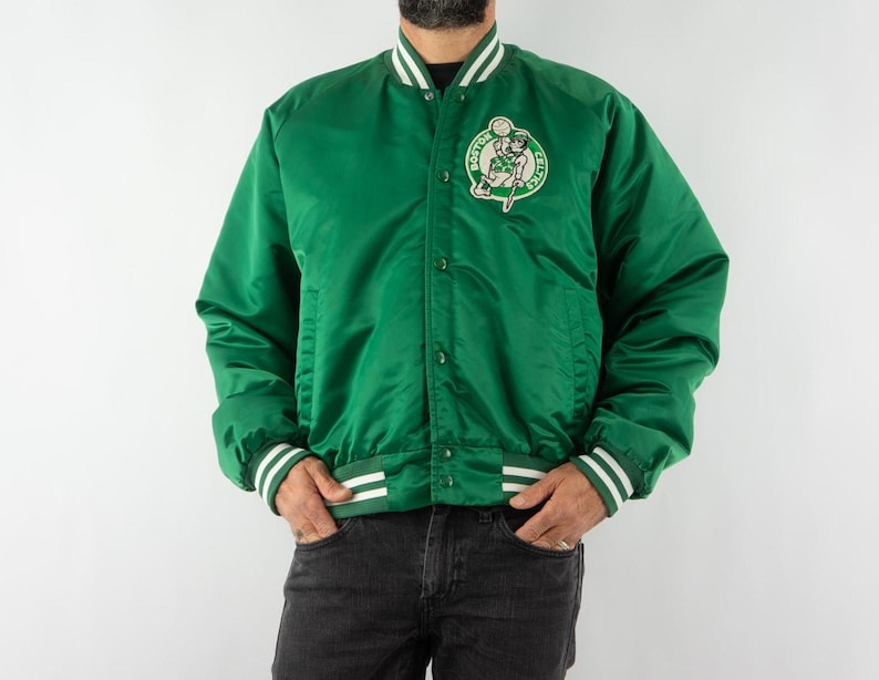 May include: A green satin bomber jacket with white and green striped ribbing at the cuffs and collar. The jacket features a large embroidered patch on the left chest with the Boston Celtics logo.