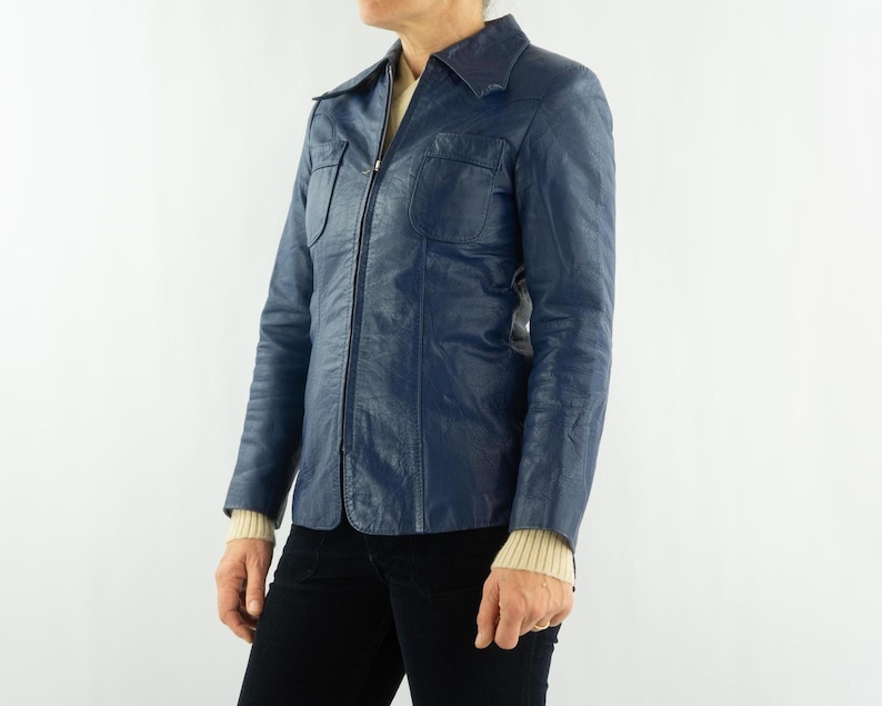 K&ouml;nnte beinhalten: Eine marineblaue Vintage-Lederjacke mit Kragen, zwei Brusttaschen und einem durchgehenden Rei&szlig;verschluss. Die Jacke hat lange &Auml;rmel und wird mit einer schwarzen Hose getragen. Die Jackenl&auml;nge betr&auml;gt ca. 71 cm.