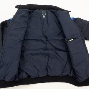 May include: A navy blue puffer jacket with a black ribbed collar and cuffs. The jacket has a zipper closure and a small pocket on the inside. The jacket has a colorful stripe pattern on the inside of the collar.