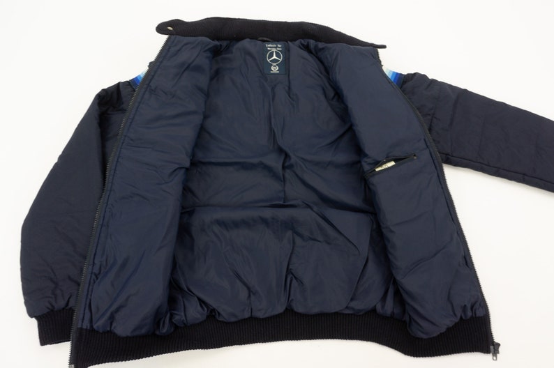 May include: A navy blue puffer jacket with a black ribbed collar and cuffs. The jacket has a zipper closure and a small pocket on the inside. The jacket has a colorful stripe pattern on the inside of the collar.