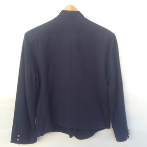 Pode incluir: Um blazer azul escuro com gola mandarim e bot&otilde;es dourados. O blazer tem mangas compridas e uma bainha ligeiramente cortada.