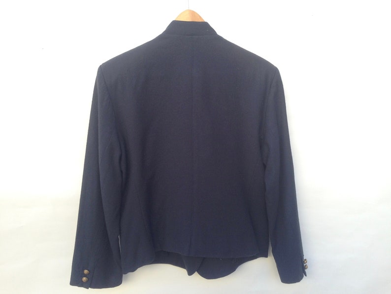 Pode incluir: Um blazer azul escuro com gola mandarim e bot&otilde;es dourados. O blazer tem mangas compridas e uma bainha ligeiramente cortada.