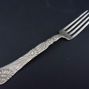 以下が含まれることがあります： 柄に花柄が施された銀製のフォーク。フォークは4本の歯と丸みを帯びた柄をしています。