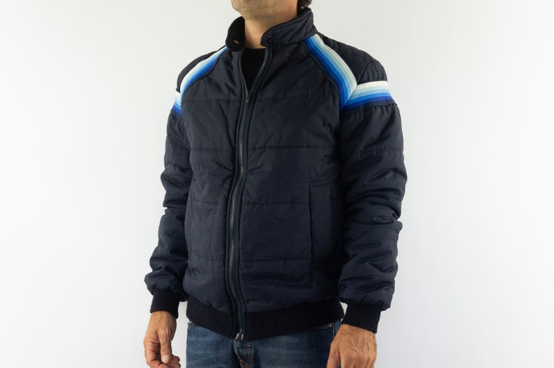 May include: A navy blue puffer jacket with a zipper closure and a striped design on the shoulders. The stripes are in shades of blue and white.