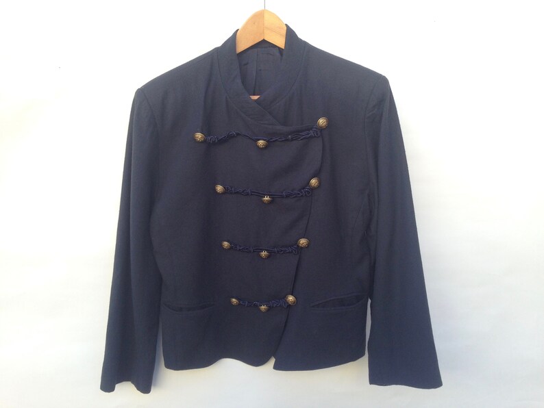 Pode incluir: Um blazer azul marinho com gola mandarim e bot&otilde;es dourados. O blazer tem um design assim&eacute;trico &uacute;nico com uma &uacute;nica fila de bot&otilde;es de um lado e uma dupla fila do outro.