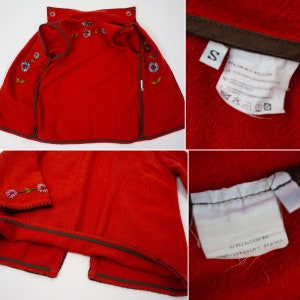 May include: Red fleece jacket with embroidered flowers and a brown zipper. The jacket has a size tag that says "S".