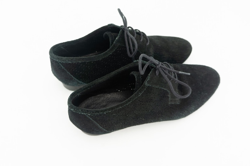 Op de afbeelding: Een paar zwarte su&egrave;de veterschoenen met een geperforeerd ontwerp.