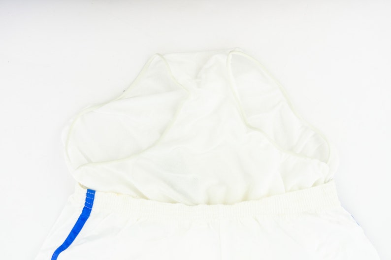 May include: White athletic shorts with a blue stripe down the side. The shorts have a built-in liner.
