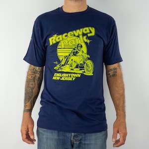 May include: A navy blue t-shirt with a neon yellow graphic. The graphic features the text "Raceway Park" above an image of a motorcycle racer and the text "Englishtown New Jersey".