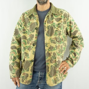 Peut inclure: Veste de camouflage avec un col vert et une fermeture boutonnée. La veste présente un motif de formes vertes, marron et beige. Elle possède deux poches avant et un style classique et décontracté.