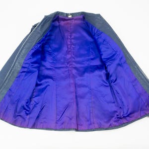 K&ouml;nnte beinhalten: Eine dunkelblaue Lederjacke mit einem leuchtend lila Satinfutter. Die Jacke ist offen und zeigt den Kontrast zwischen Au&szlig;en- und Innenseite. Das Futter hat einen Farbverlauf, der von Lila zu einem tieferen Farbton &uuml;bergeht.