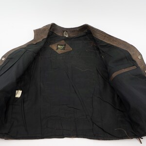 May include: Open view of a brown leather vest with a black interior lining. The vest has a button-up front, two interior pockets, and a small tag. The leather has a distressed appearance.