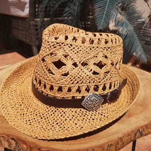 A straw hat with a metal buckle is placed on a wooden table.