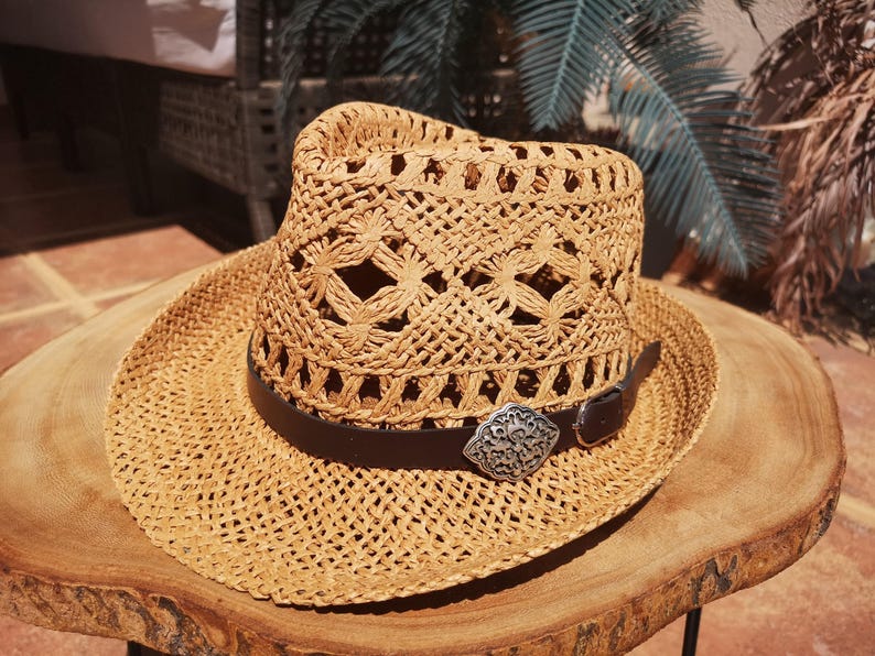 A straw hat with a metal buckle is placed on a wooden table.