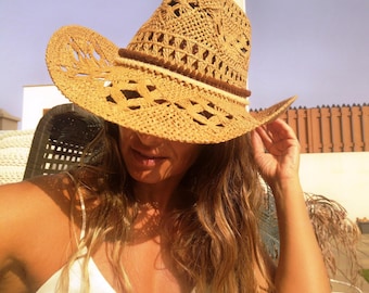 Puede incluir: Sombrero de vaquero de paja tejida con ala ancha y ribete marrón decorativo. El sombrero presenta un diseño de tejido abierto, que permite la ventilación. El sombrero es de color marrón claro y parece hecho a mano.
