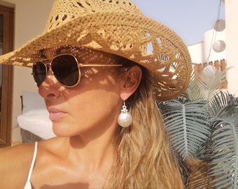 May include: A pair of round, white, spherical drop earrings featuring a silver-toned metal cap at the top. The earrings are worn with a tan woven straw hat and gold-framed aviator sunglasses with dark lenses, creating a bright, sunny aesthetic.