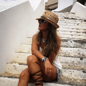 A woman wearing a straw hat and sunglasses sits on a set of stairs, looking off to the side.