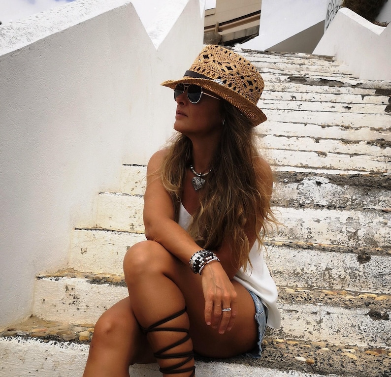 A woman wearing a straw hat and sunglasses sits on a set of stairs, looking off to the side.