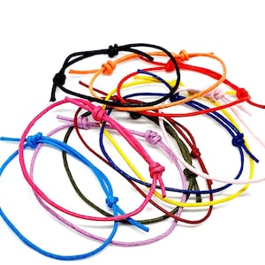 Peut inclure: Un ensemble de bracelets en corde de différentes couleurs, notamment bleu, rose, rouge, jaune, vert et noir. Les bracelets sont noués et disposés en pile.