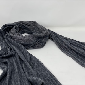 Könnte beinhalten: Ein grauer gerippter Strick Schal. Der Schal ist in der Hälfte gefaltet und liegt flach auf einer weißen Oberfläche.