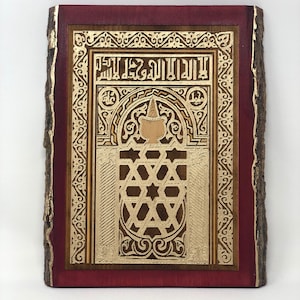 May include: A wooden wall hanging with a red frame and a gold-colored design. The design features intricate geometric patterns and Arabic calligraphy.