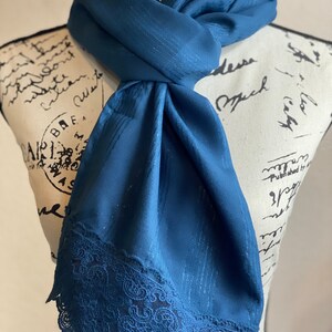 May include: A teal blue scarf with a lace trim. The scarf is made of a soft, silky fabric and has a subtle sheen.