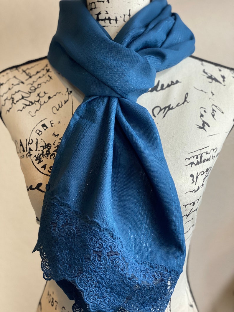 May include: A teal blue scarf with a lace trim. The scarf is made of a soft, silky fabric and has a subtle sheen.