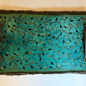 May include: A teal wooden serving tray with a black and gold leaf design and brass handles.