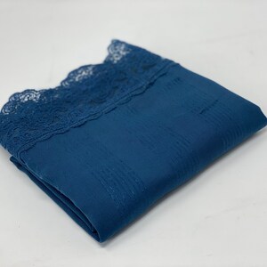 May include: A folded blue fabric with a lace trim. The fabric has a subtle texture.