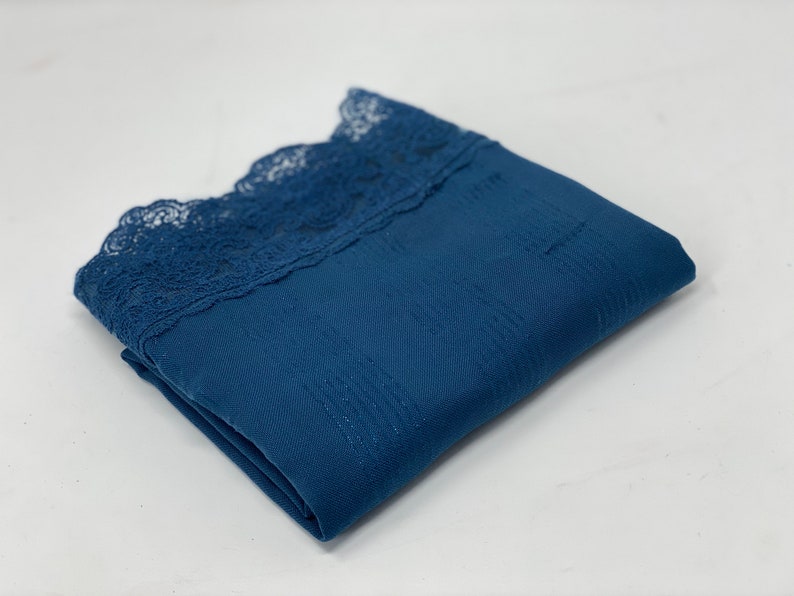 May include: A folded blue fabric with a lace trim. The fabric has a subtle texture.