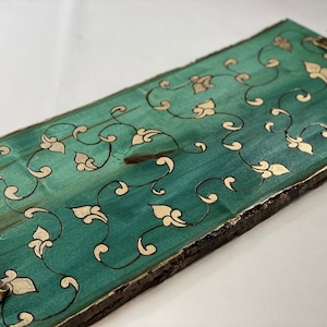 May include: A rectangular wooden serving tray with a teal green finish and gold leaf floral design. The tray has a natural wood edge and two brass handles.