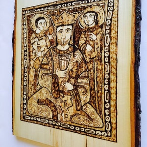 May include: A woodburned image of a king with a crown, holding a scepter, and two figures standing behind him. The image is framed with a decorative border.